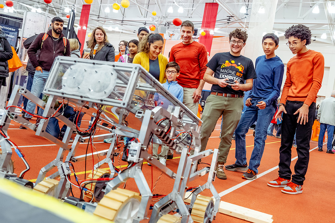 students are shown gathering around a robot that is on display at ImagineRIT.