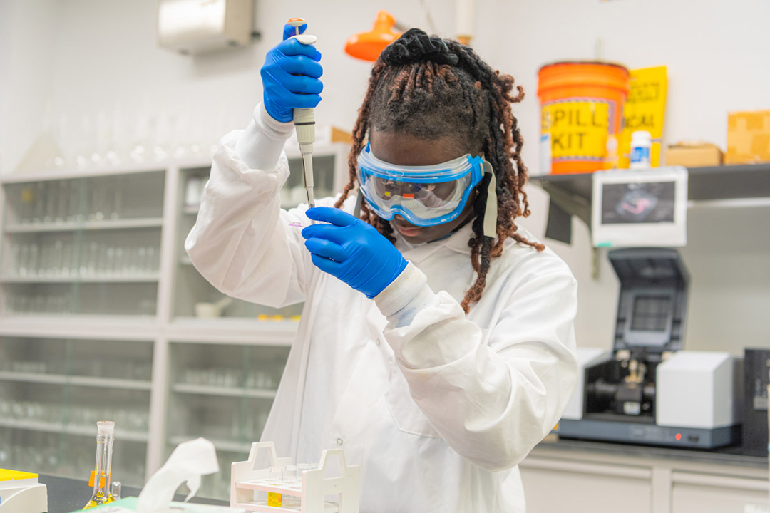 Maameyaa Asiamah is shown in a lab coat using a pipette on science materials.
