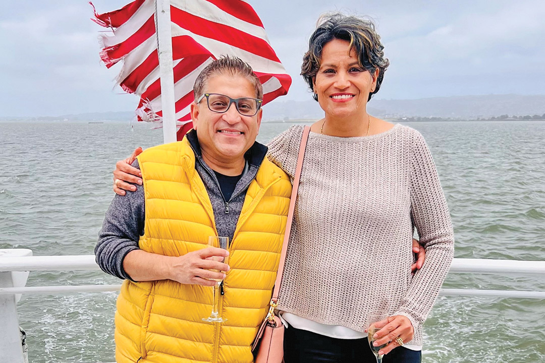 Deepak Sharma and Karuna Mukherjea stand together on a boat that is sailing in open water.