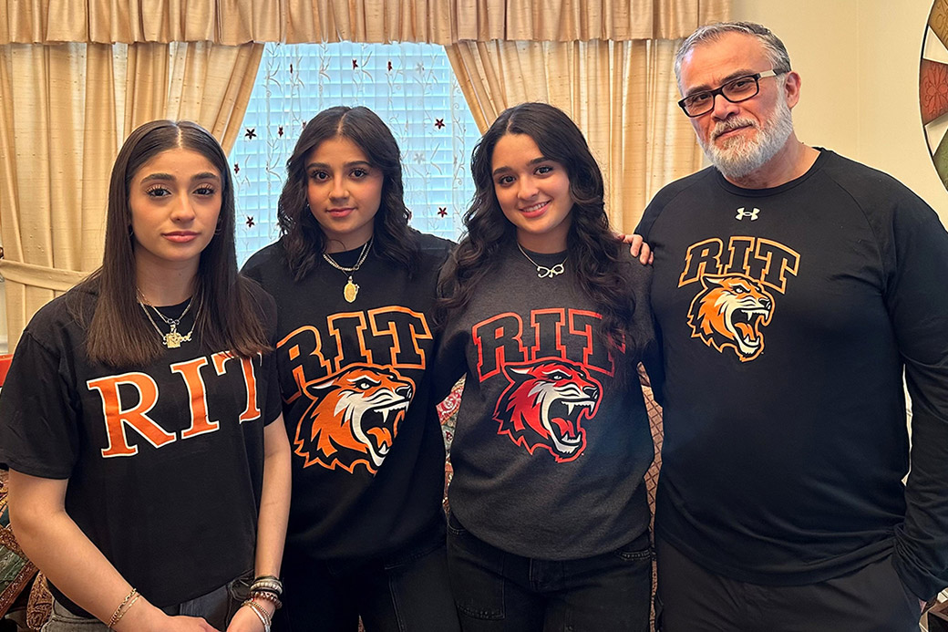 a family stands in a livingroom all wearing R I T shirts.