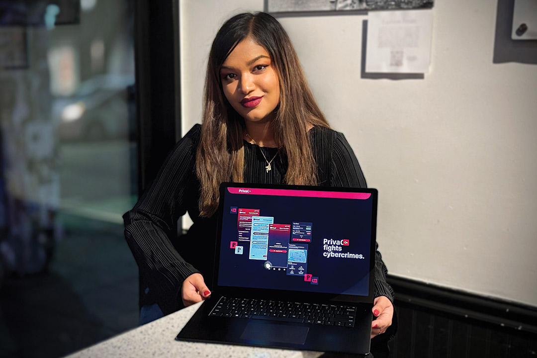 Nuzhat Minhaz sits on a table holding a laptop that is open to a screen displaying information about her company called Priva C.