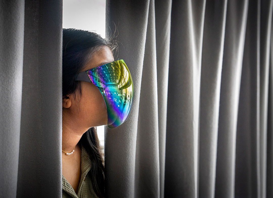 a person is show peeking out from curtains wearing a reflective face mask as a part of the show.