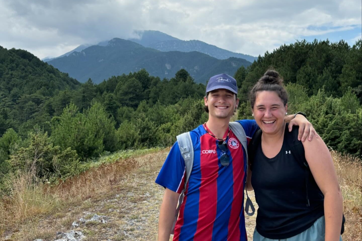 Siblings pose for photo on trail with mountains in the background.