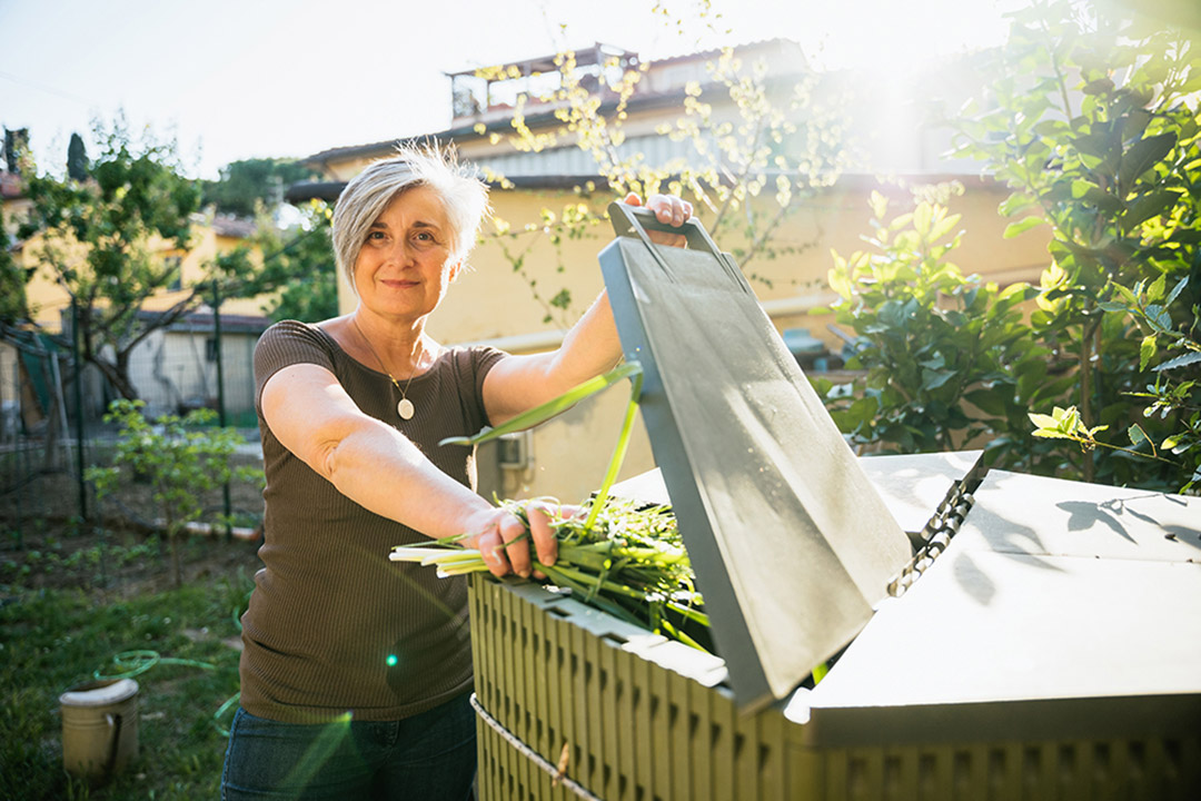 a woman in a green shirt opens the top of a compost bin.