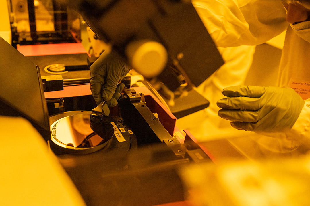 an amber colored photo shows a researcher taking a round chip off a plate.