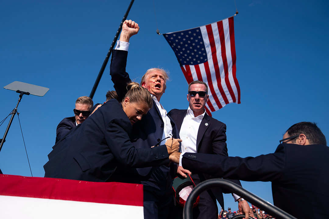 Donald Trump holds his hand up in a fist as he is taken off the stage by bodyguards after a failed assasination attempt.