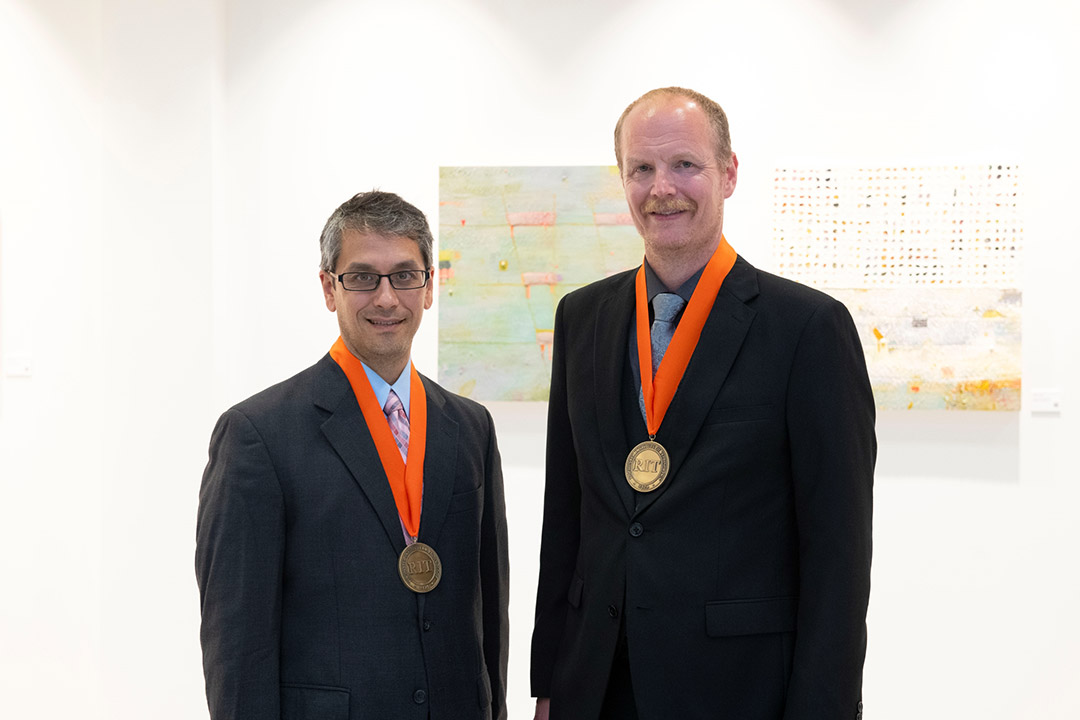 Matthew Wright, left, and Billy Brumley stand in a brightly lit room in black suits with orange and gold medals hanging from their neck.