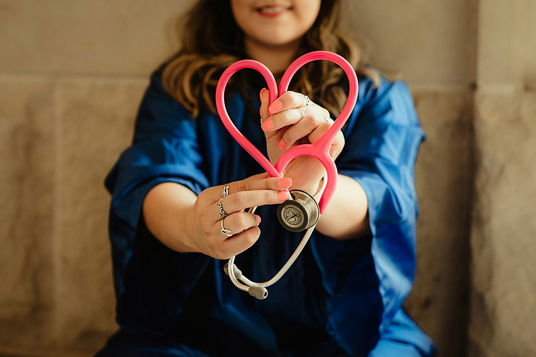 'the torso of a woman in a blue robe holds a stethoscope with a red rubber look formed in to a heart.'