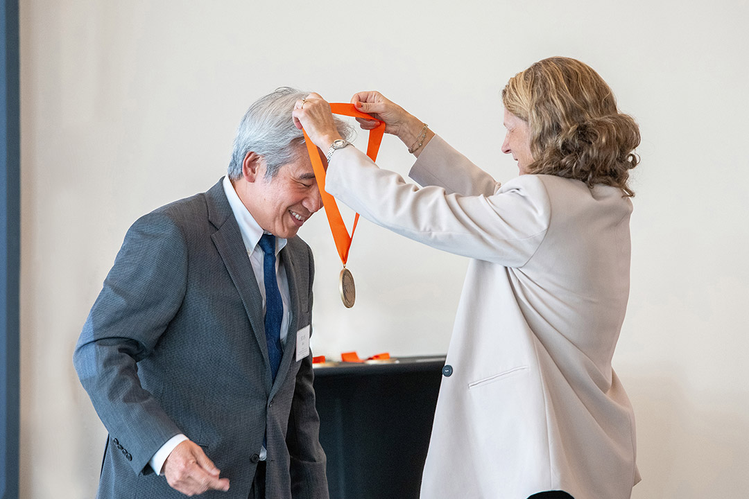 A man in a suit bends to receive a medal.