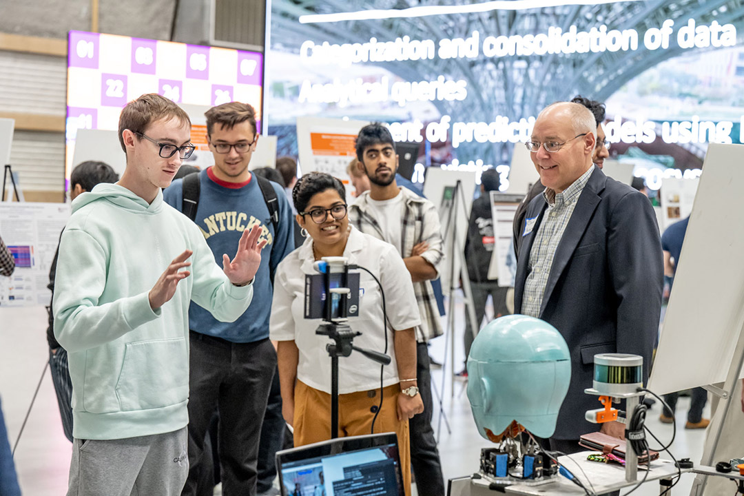 Students stand around an AI booth at a symposium.