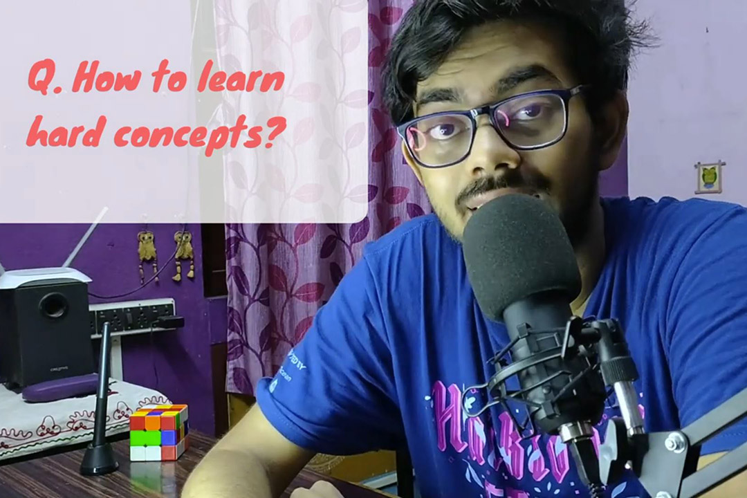 'a young man with dark hair and glasses appears in a home office with a microphone in front of him. A text box in the upper left of the image reads How to learn hard concepts.'