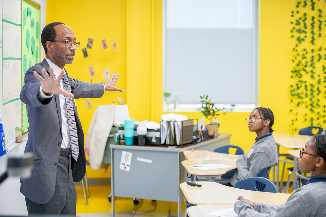 Clayton Turner stands in front of a classroom full of students gesturing with his arms wide.