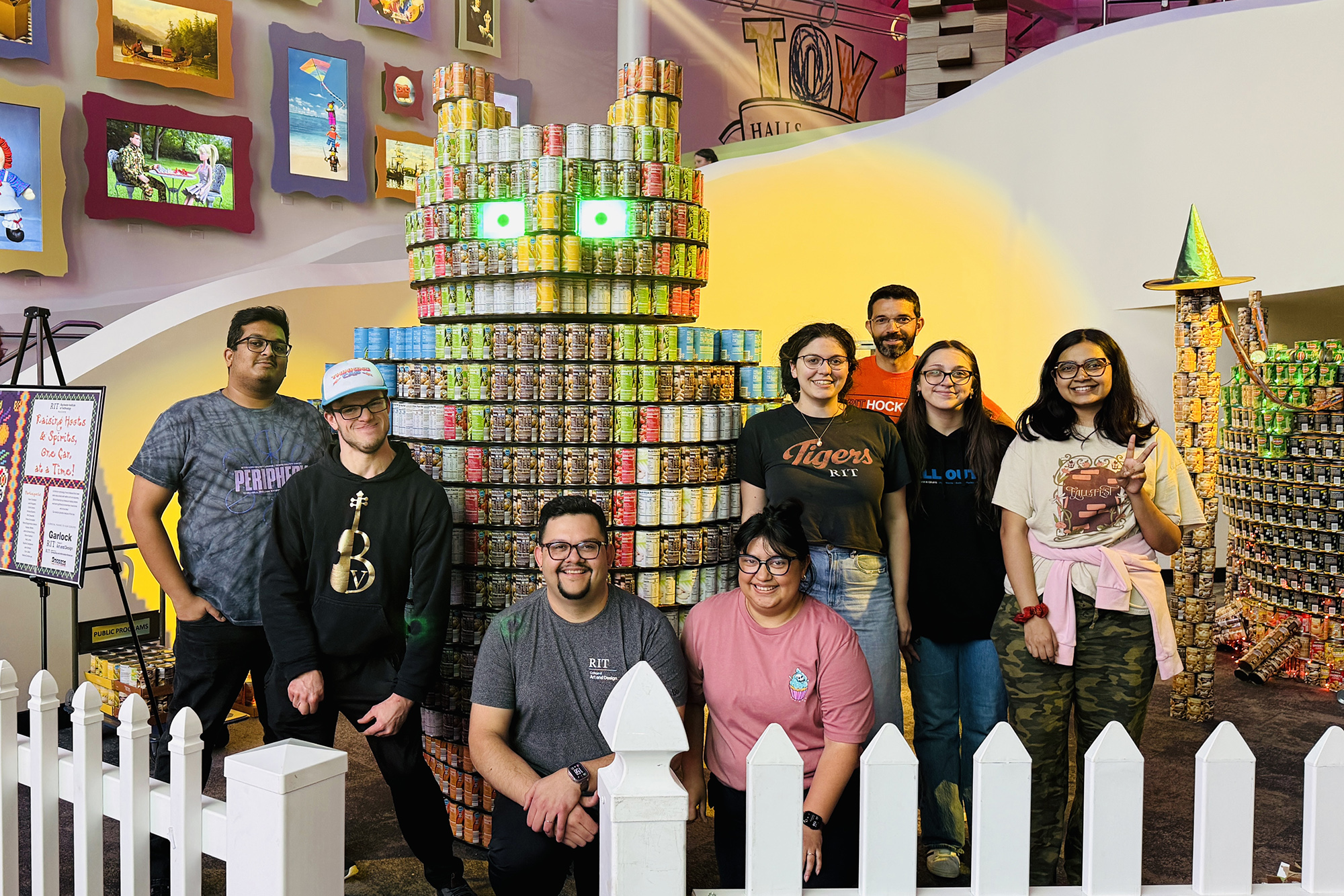 A group of students stand around an owl sculpture made out of canned food.