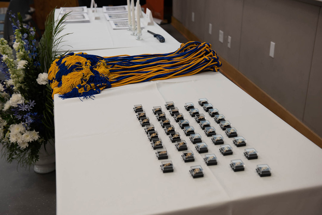 a table with graduation items for a Greek fraternity, including individually boxed pins and blue and yellow cords.