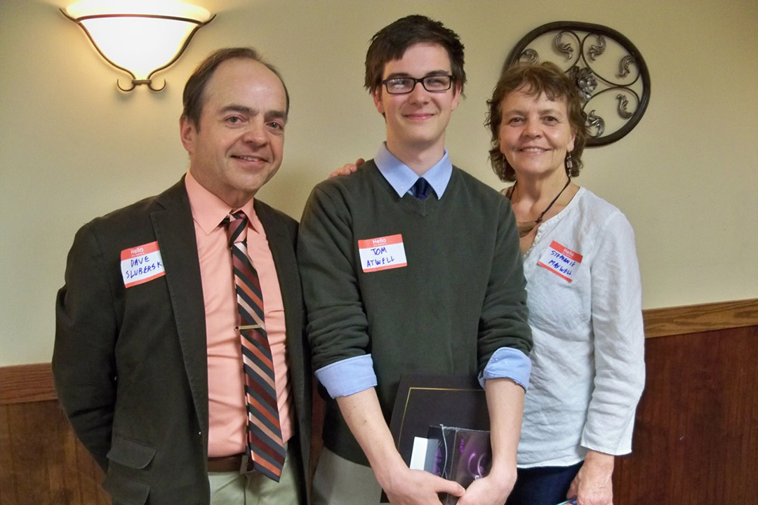 Tom Atwell stands with his parents to both his sides while holding the award.