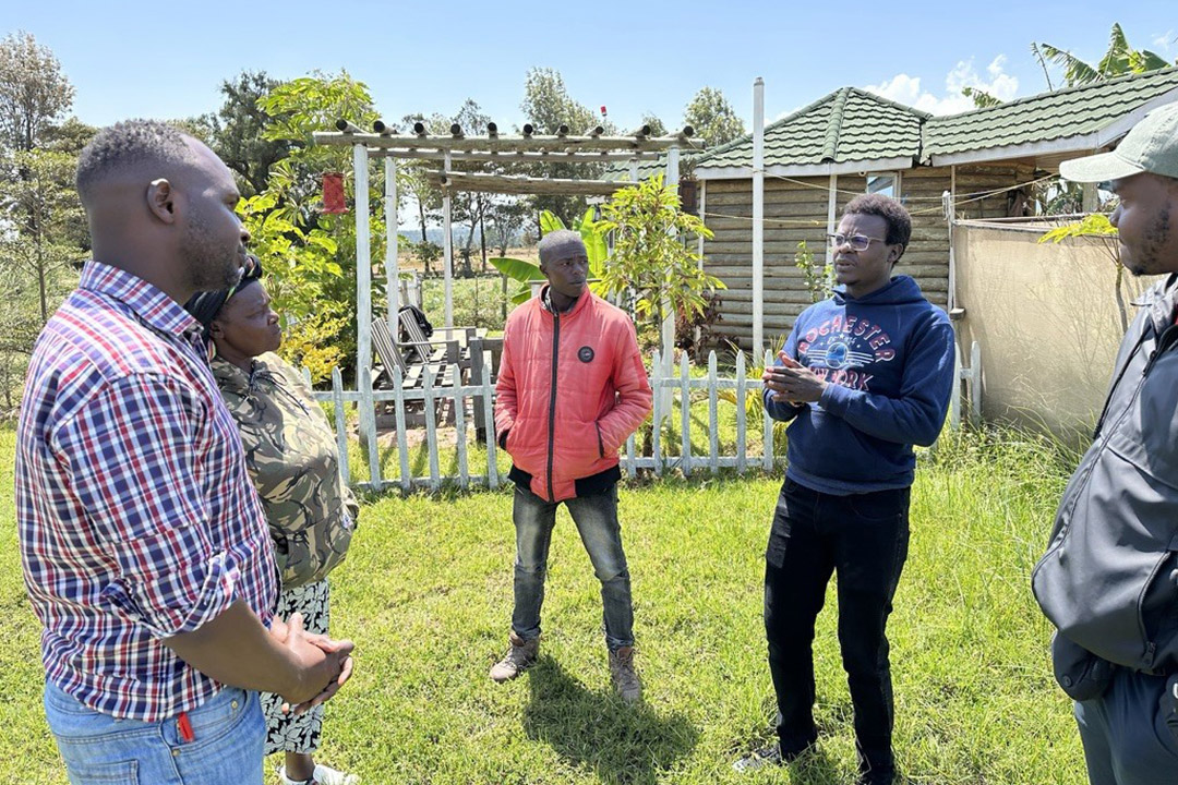 Five black men stand in a semicircle in a small garden in Kenya.