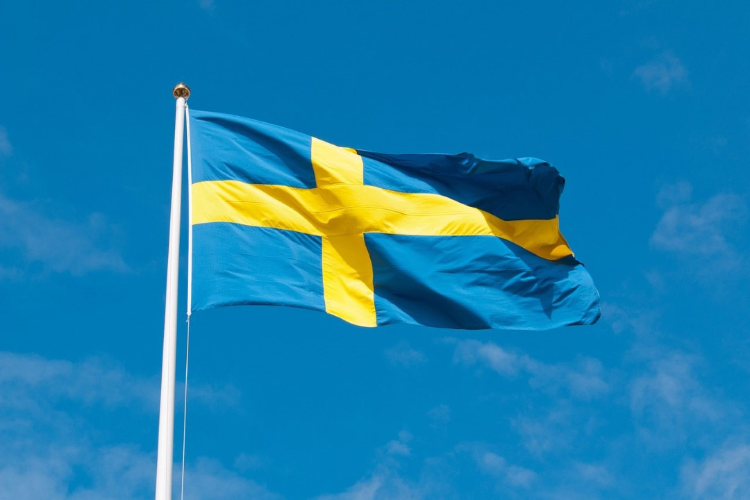 'The blue and yellow flag of Sweden appears in a blue sky.'