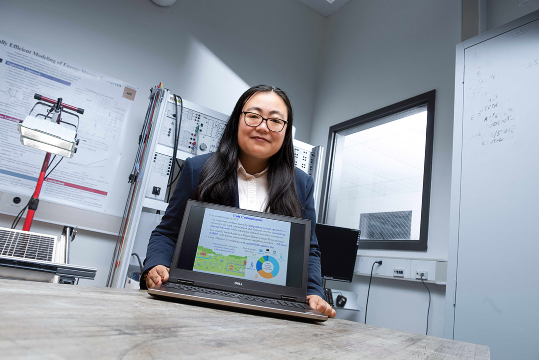 Bing Yan holds a laptop in front of themselves in a lab room.