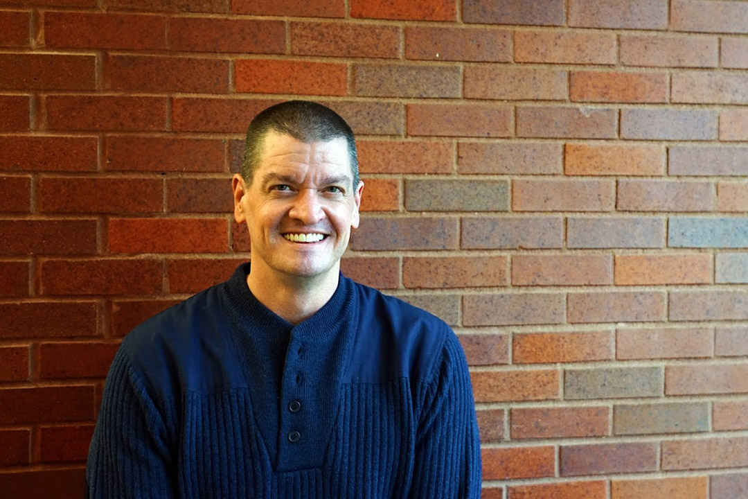 Chris Soukup stands in a blue shirt against a brick wall.