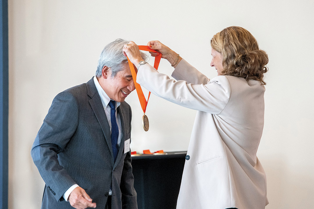 a adult man leans forward to accept a medal on an orange ribbon being presented by an adult woman.