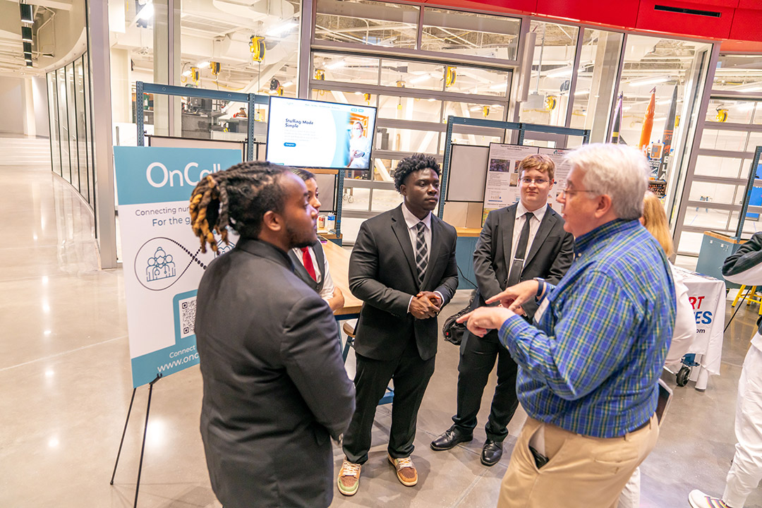 From left, students Joshua Michaels (marketing), Nemesis Velasquez (new media interactive development), Emmanuel Boakye (individualized studies), and Chad Chapman (computer science) chat with coaches Susan Ramsey and James Ramsey ’86 (accounting) about their company, OnCall,