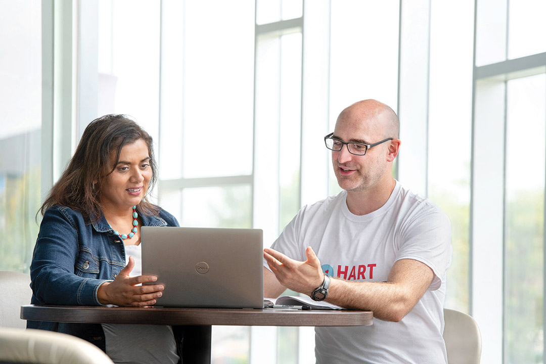 a woman and man sit and look at a laptop in a bright windowfilled space.