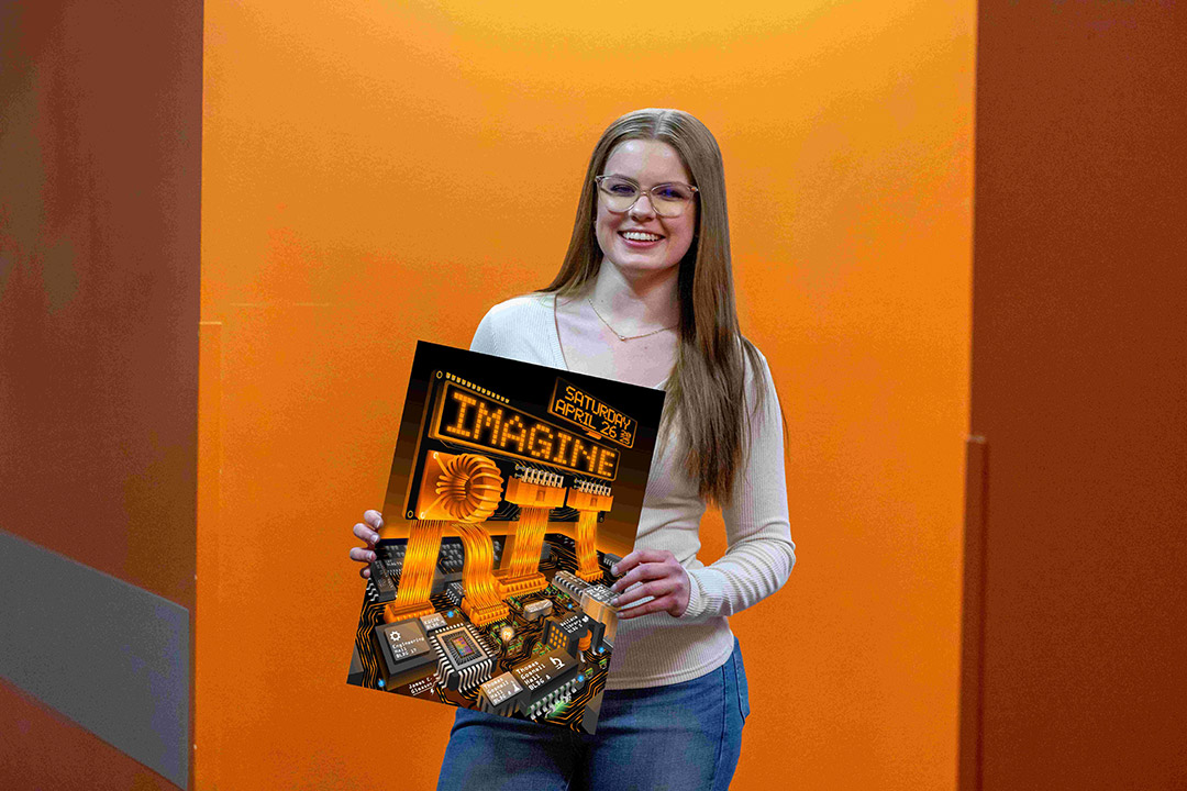 Smiling woman with long blonde hair and glasses holds a poster for 'Imagine RIT,' featuring a circuit board design with glowing orange text. She stands against an orange-toned background.