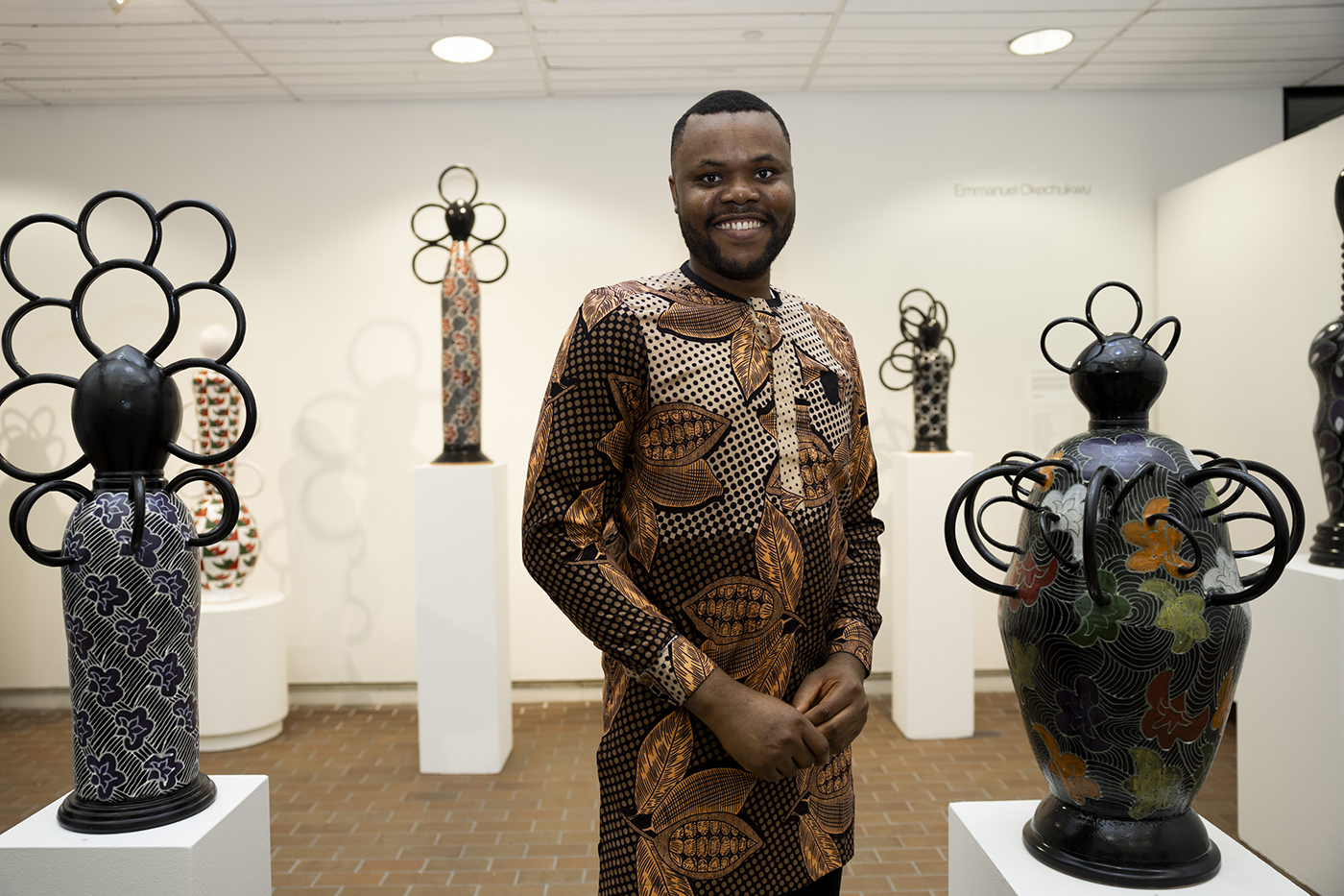 Emmanuel Okechukwu stands beside ceramic sculpture he made for this thesis exhibition.