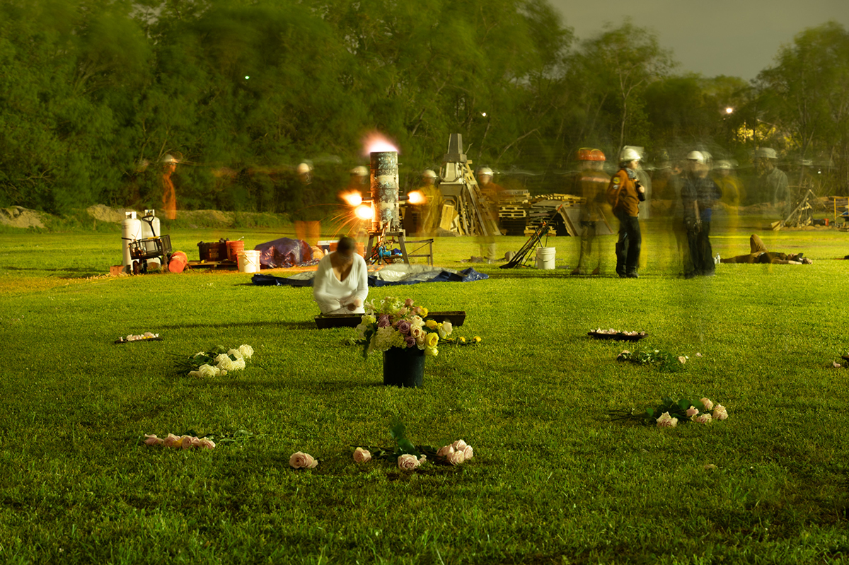 Elizabeth Kronfield places flowers in a container while a molten iron furnace operates in the background.