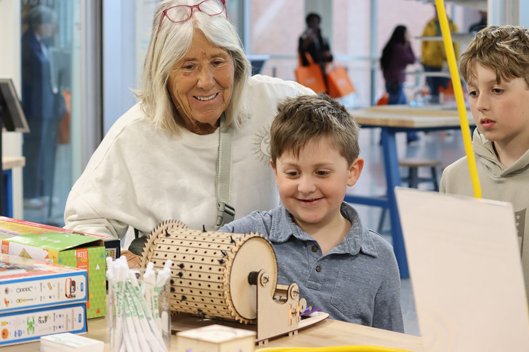 young boy delighted by music making machine at Imagine RIT, with his grandmother looking on.