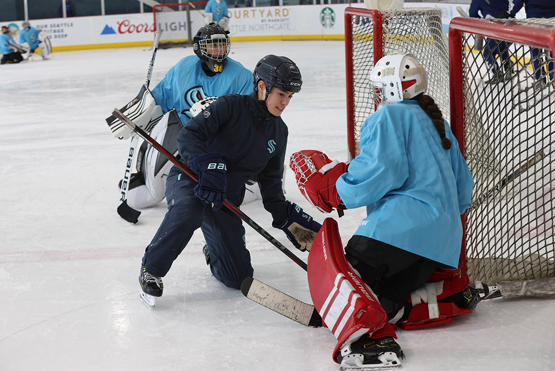 Hockey player attempts to score as goalie blocks with red pads during practice.