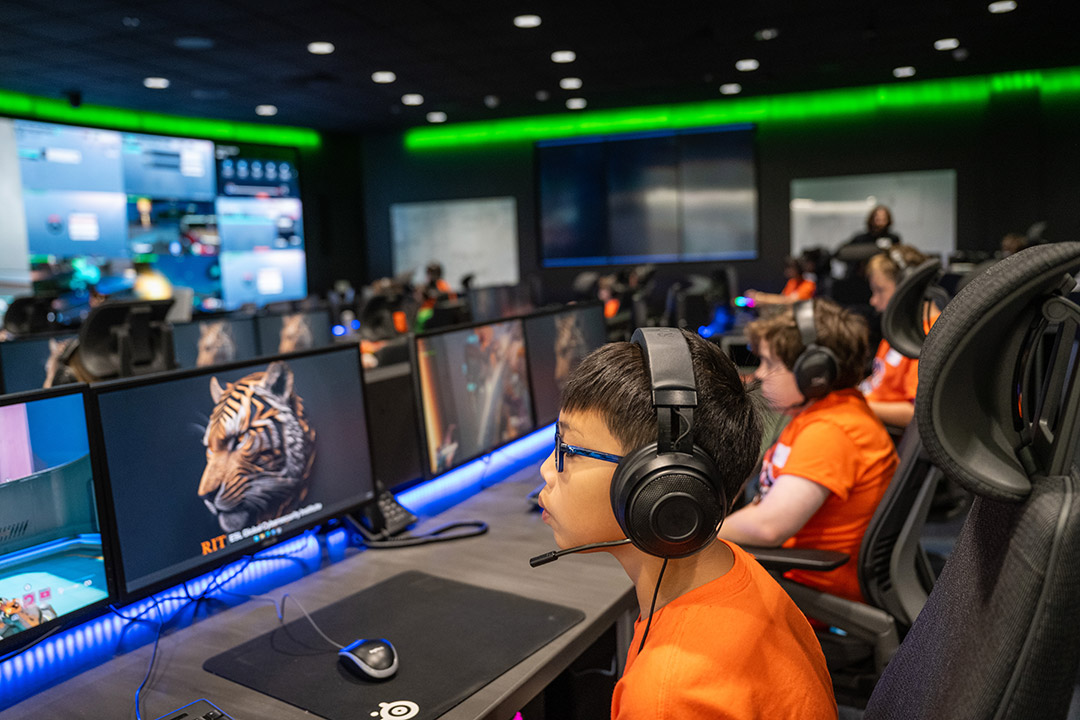 young students sit in a computer lab using a program and wearing headsets.