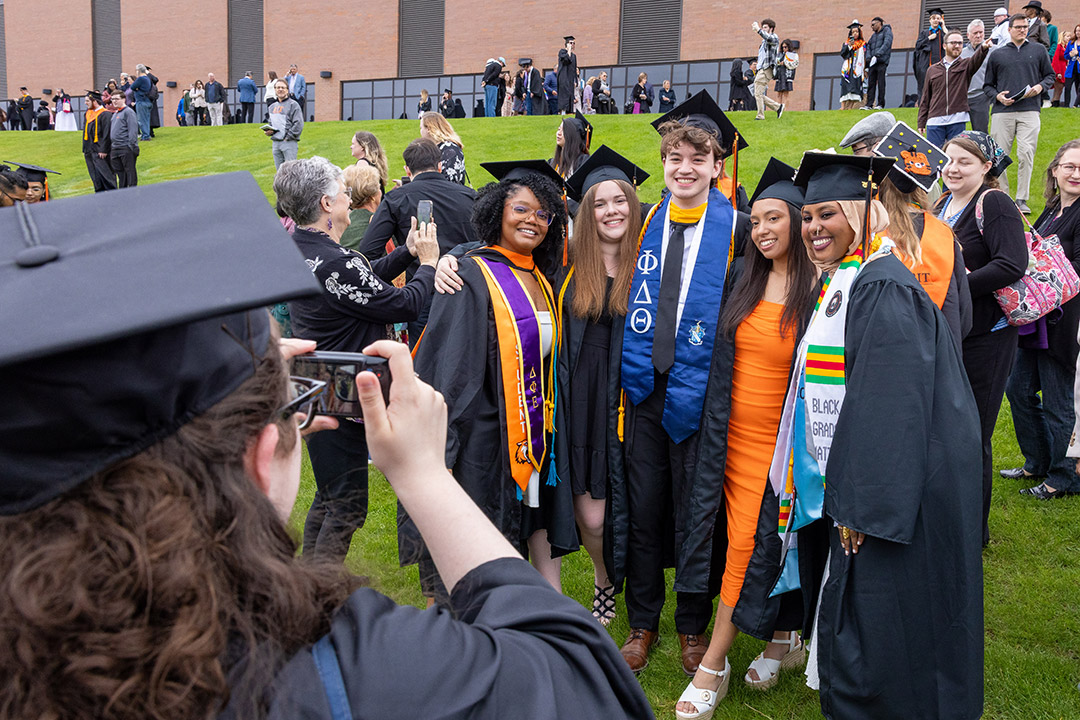 Graduates in caps and gowns pose for a group photo on a lawn during a commencement celebration.
