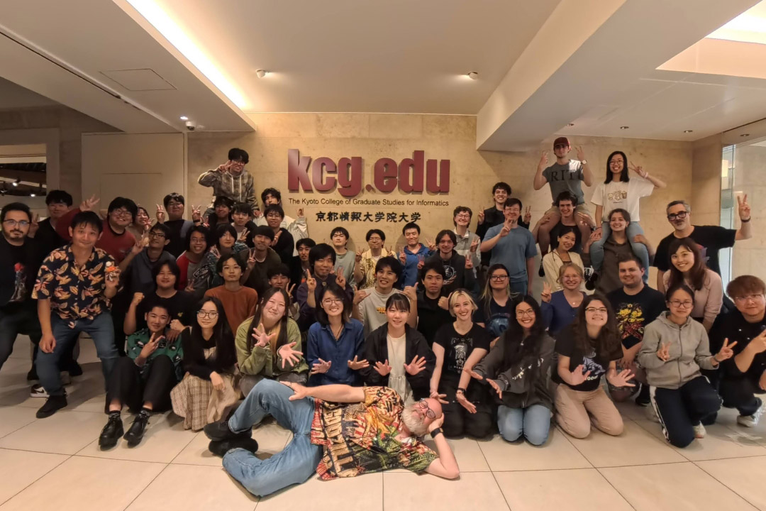 Large group of international students posing indoors at Kyoto College of Graduate Studies for Informatics.