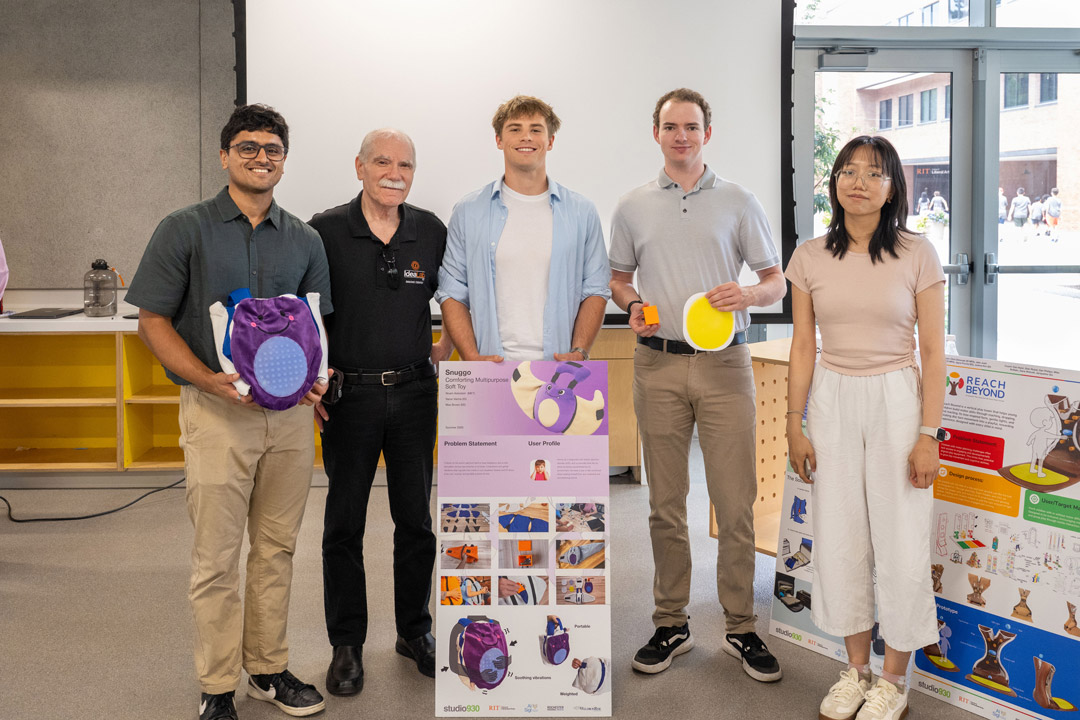 Four students stand with a professor showing a poster and products they created.