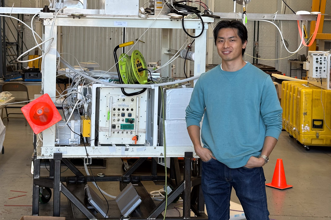 student Kazuma Noda stands with the BOOP! gondola in a warehouse setting.