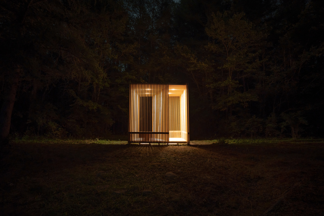 A wooden structure is illuminated at night amongst trees.