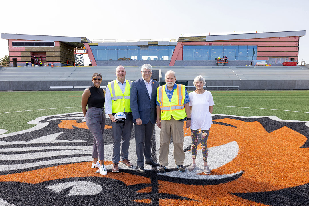 'Five people standing on a sports field with a construction site in the background.'