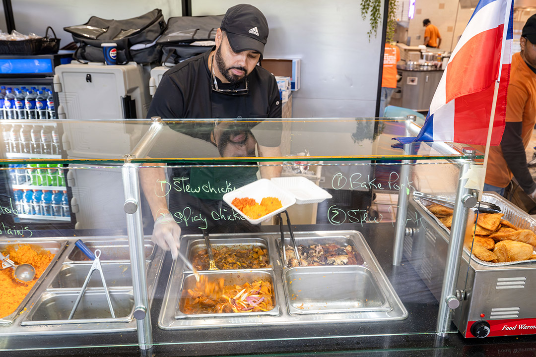 a man in a black hat scoops food from behind a glass barrier