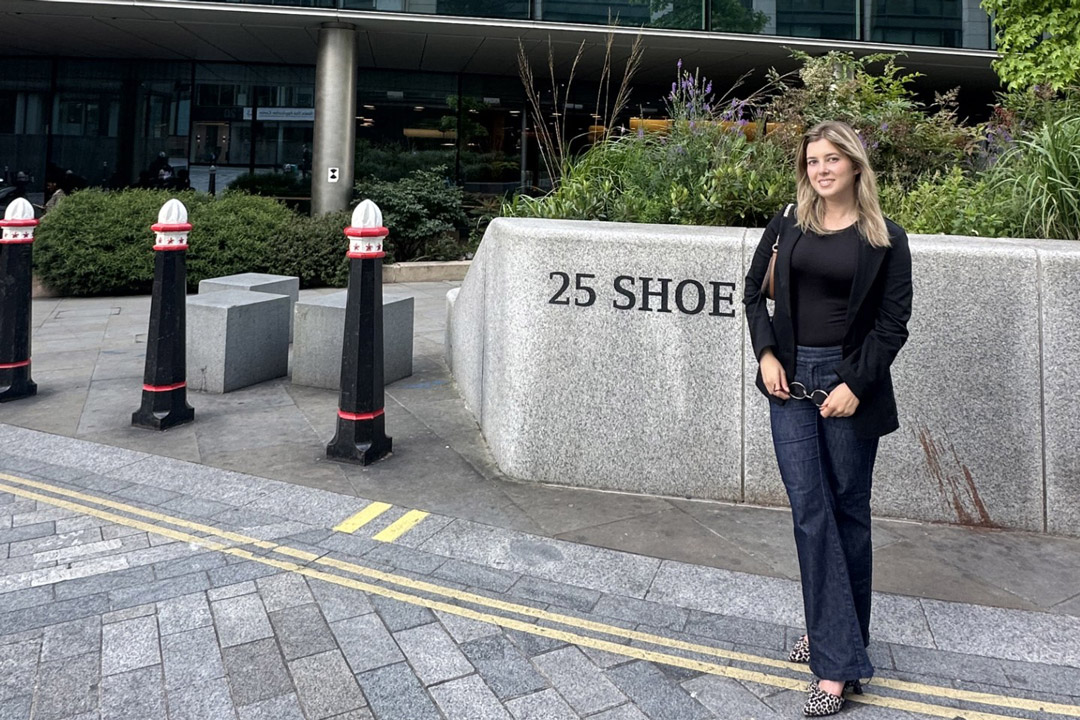 a woman dressed in a black top and jeans stands in a public plaza.