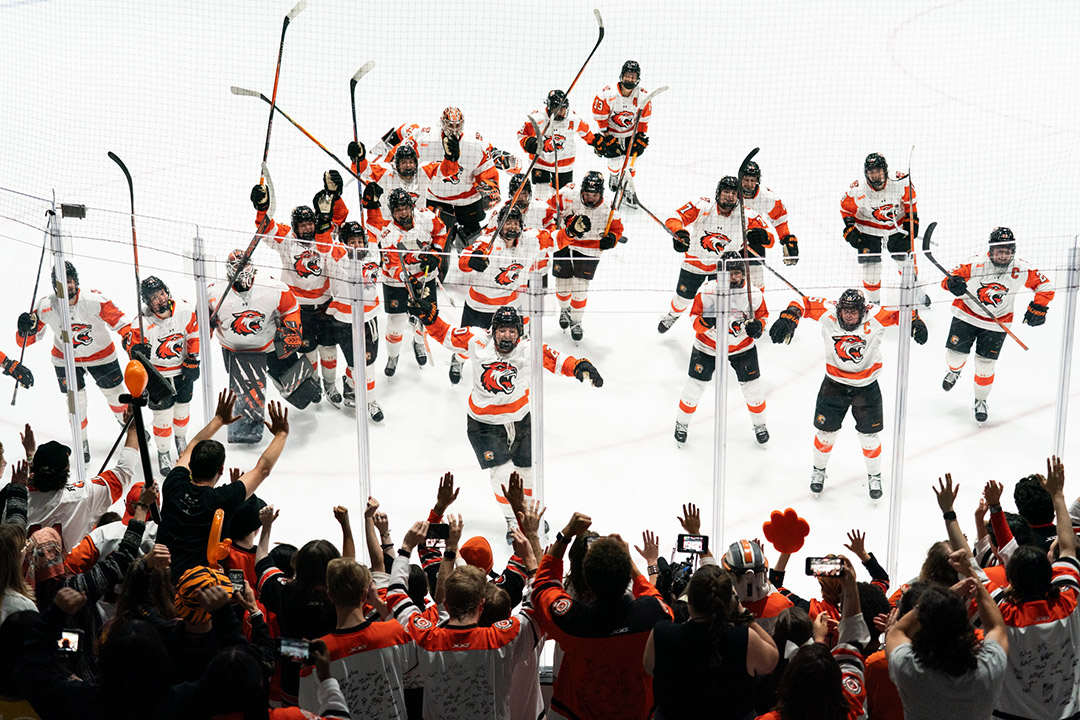 'the R I T womens hockey team celebrates with sticks up on the ice.'