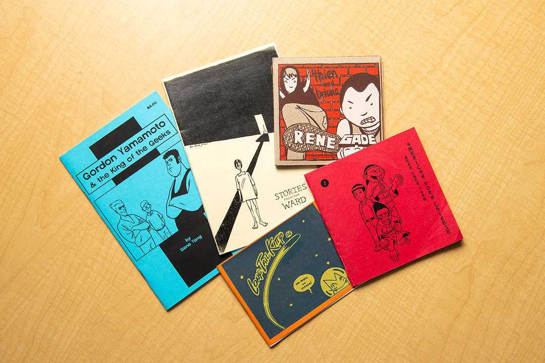 a collection of graphic novels are spread on a wood tabletop.