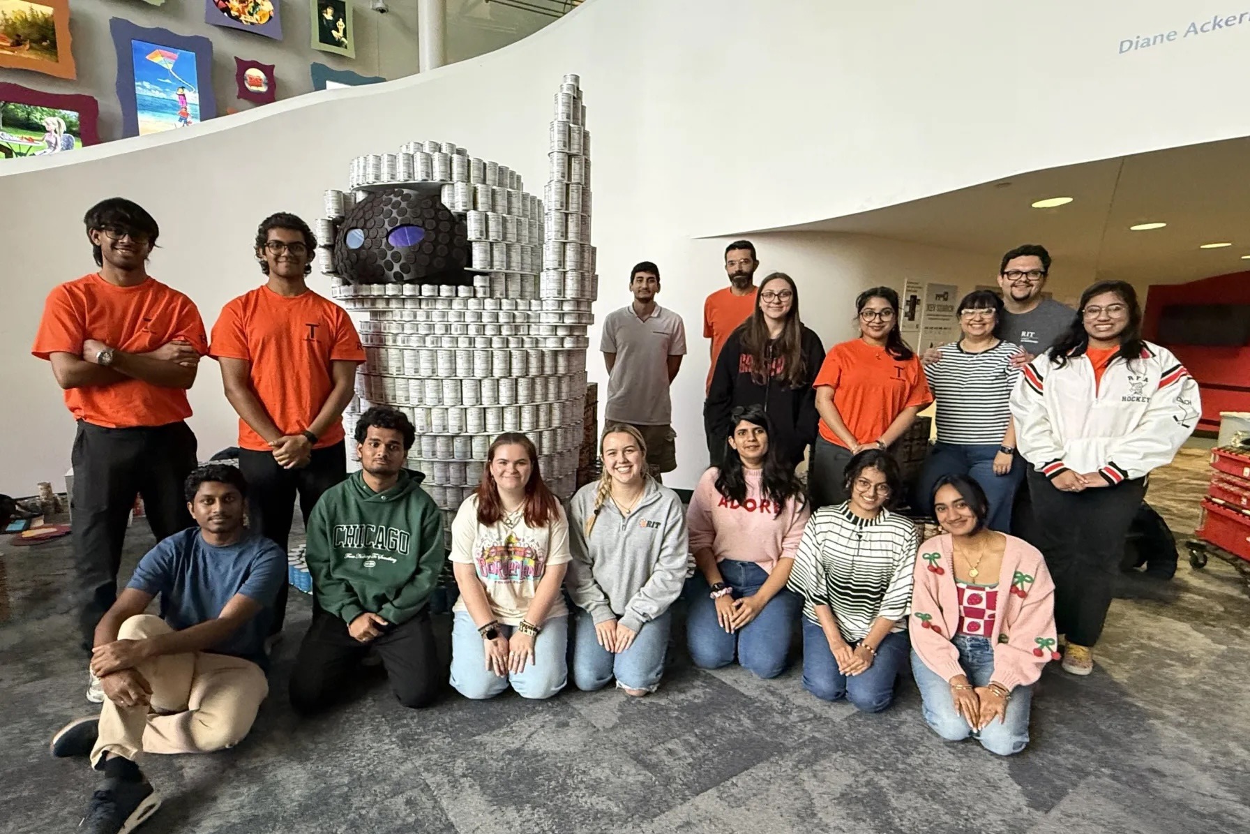 RIT students gathered around a sculpture of EVE from WALL-E, built entirely out of canned food