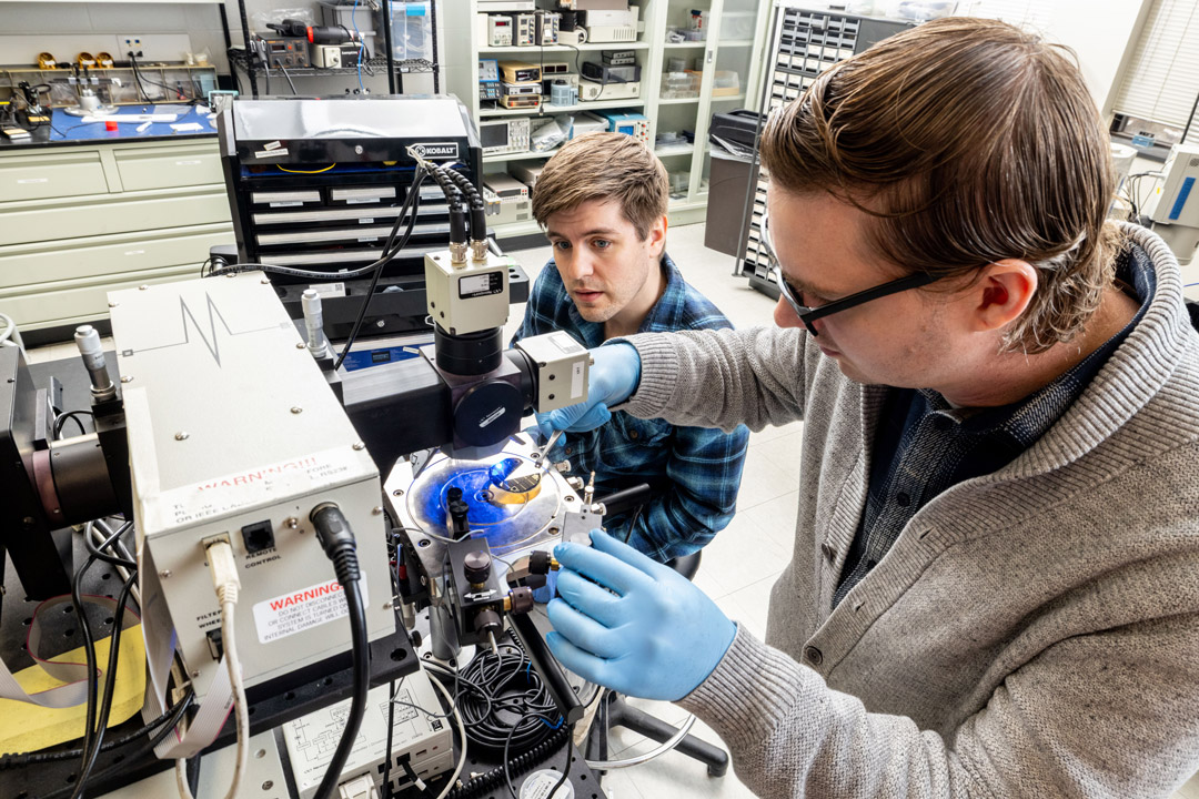 'two men in a lab environments use a machine for semiconductors.'