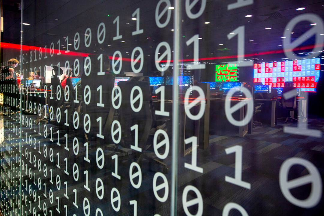 'a transparent wall reflecting computers is covered in decals of ones and zeroes.'