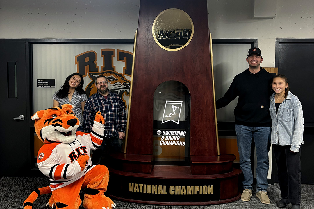 Students and a tiger mascot pose by a large trophy.