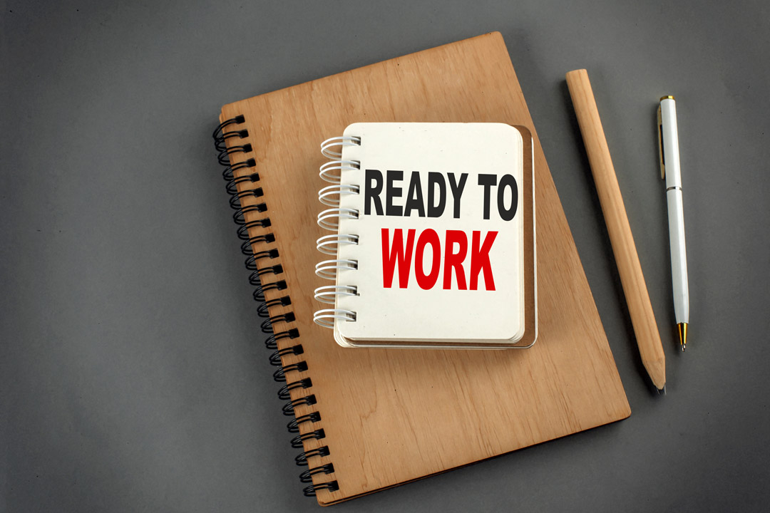 'a stock image of business supplies on a gray background including a notebook that says Ready to Work.'