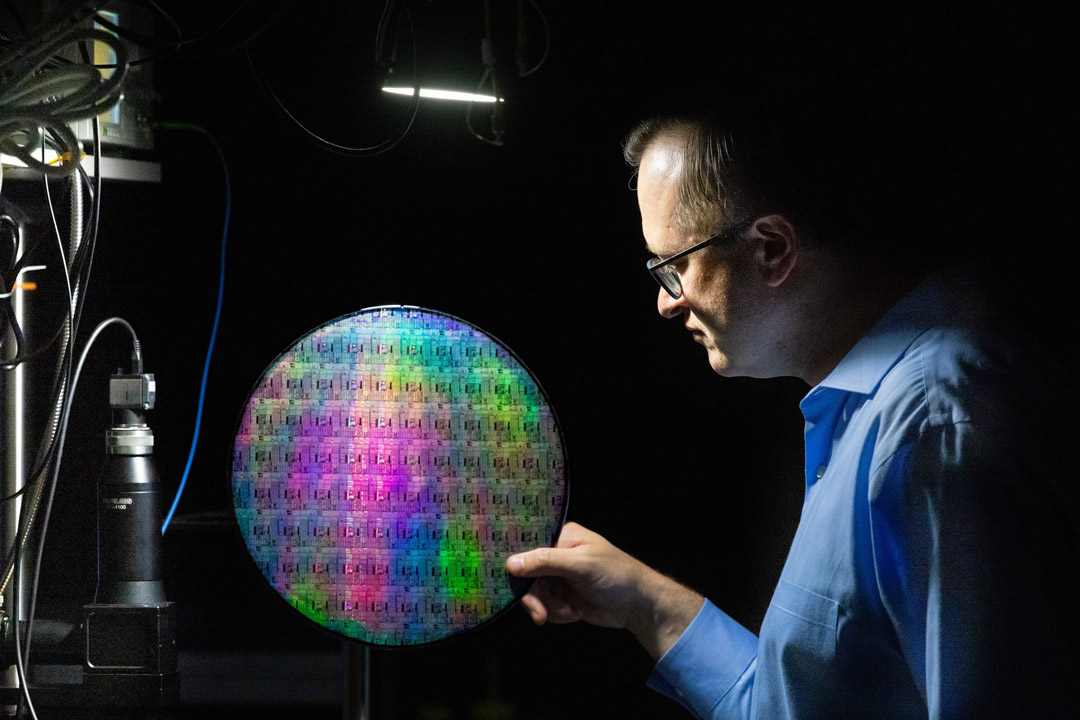 'a man in profile holds a quantum photonic wafer against a black background.'