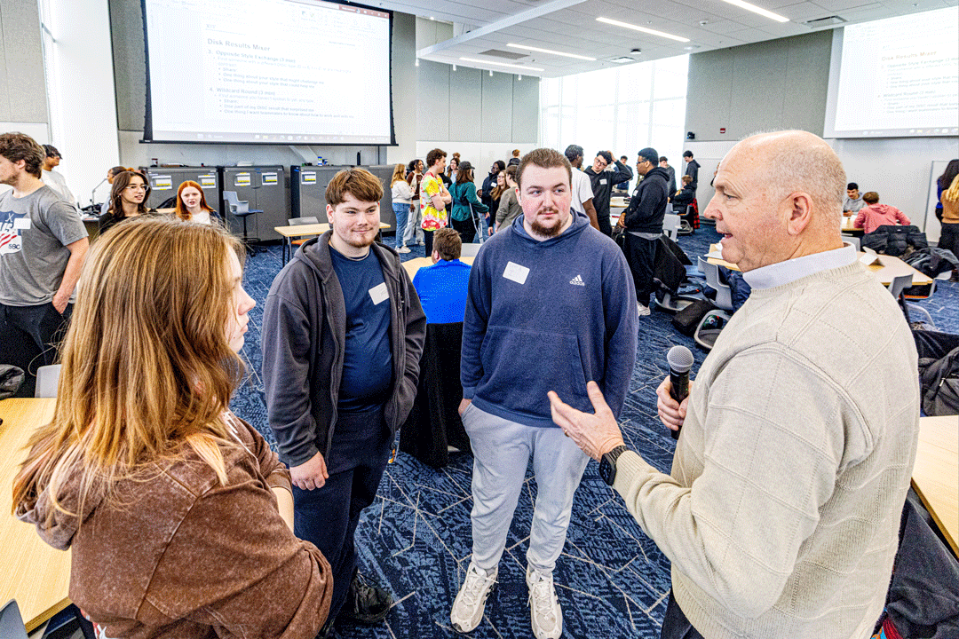 'A group of four people stand speaking in a business classroom.'