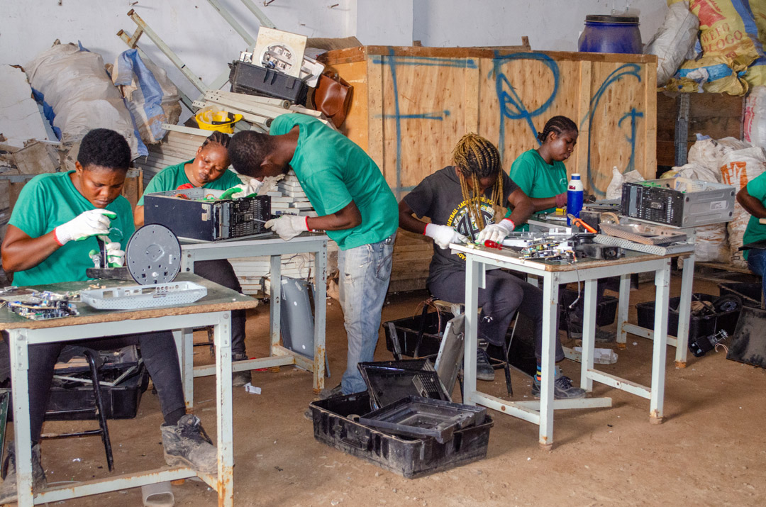 'People work at a small tables at an electronic recycling facility.'